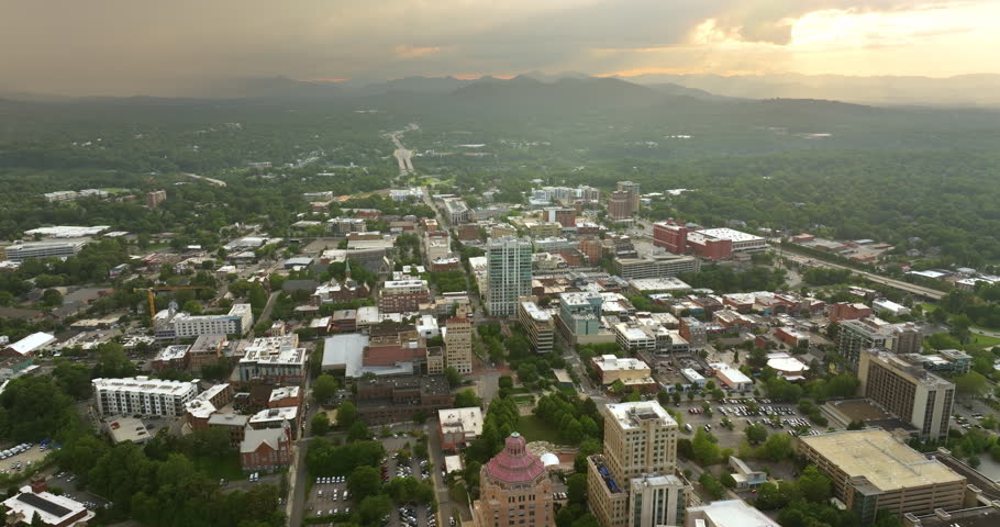 Panoramic aerial view of North Carolina Appalachian city Asheville with downtown architecture and Blue Ridge Mountain hills in distance at sunset. US travel destination Royalty-Free Stock Footage #1110117025