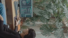IT developer scrolling through computer code on PC screen, working at desk in a modern home office with a backyard garden view. Vertical format clip