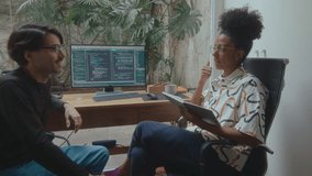 Female programmer making notes and discussing IT project with male coworker while working together in home office with PC and laptop on desk, computer code displayed on monitor - Powered by Shutterstock - Get 15% off with code: PIKWIZARD15