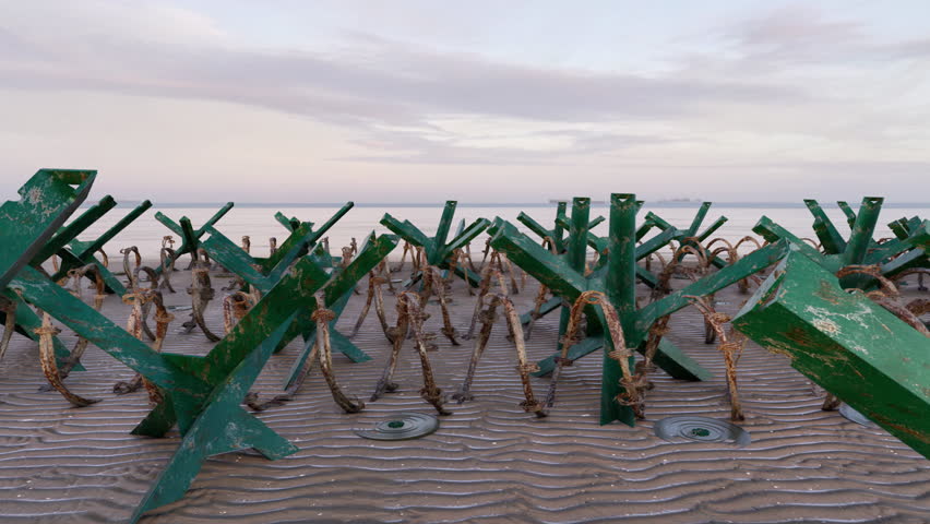 Moving behind the metal anti-tank hedgehog obstacles, landmines, and barbed wire, placed on a beach to defend against a military invasion by water.