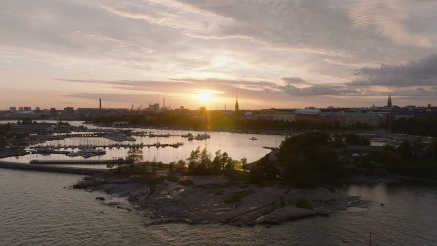 Forwards fly above cove with city marina. Silhouette of building and tall church tower against color sunset sky. Helsinki, Finland