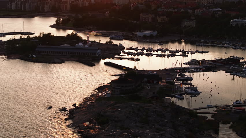 High angle view of marina and water surface reflecting sunset sky. Tilt up reveal of cityscape. Helsinki, Finland