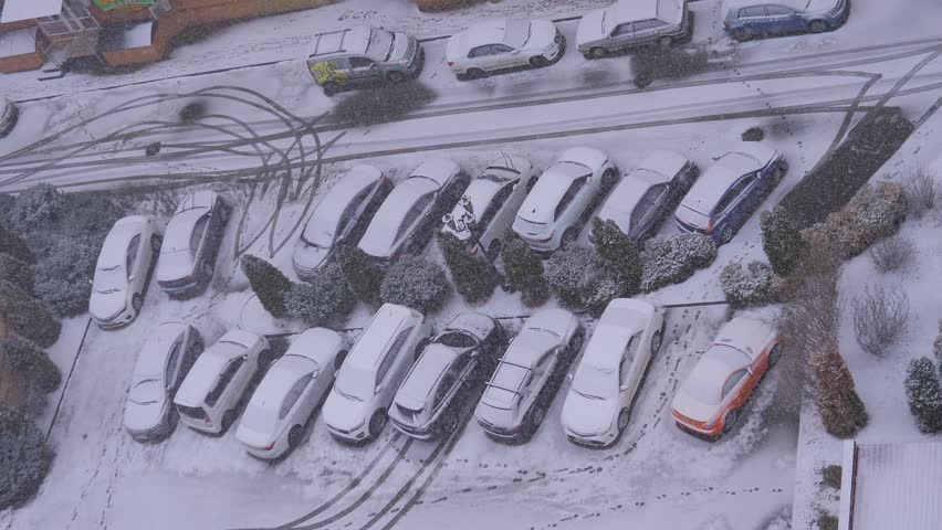 Heavy snowfall on city street, cars covered with white snow. Winter weather. Snowstorm in city, urban landscape. Snow falling in cold, frost day. Storm climate. Snowy road exterior. Buildings in ice.