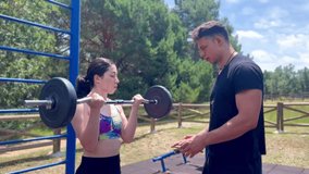 video of personal trainer correcting a girl's posture while doing the biceps curl exercise outdoors