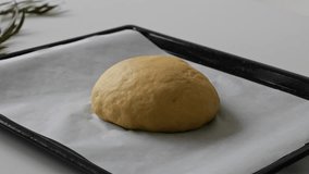 Flattening a flour dough into a circle shape on a white color baking sheet by using fingers