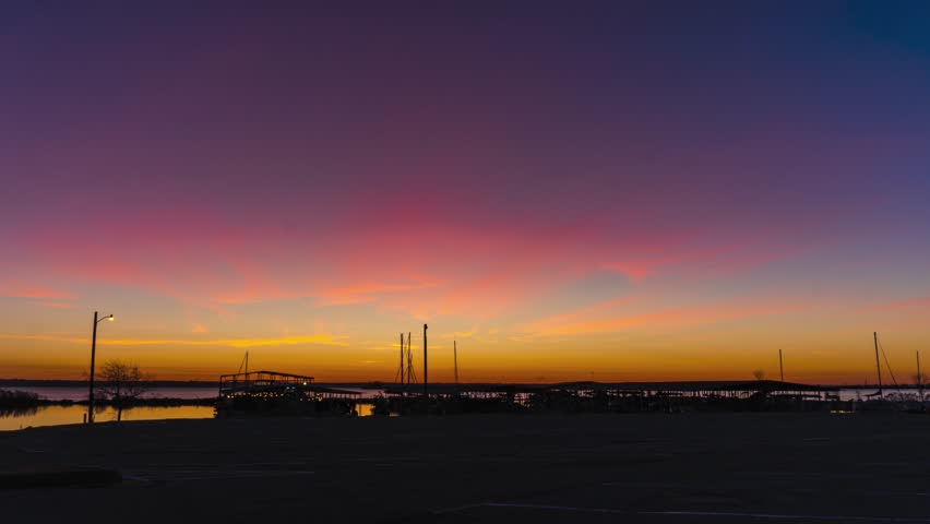 Person walks to boat house at early morning, sun rises and shines rays between ship masts