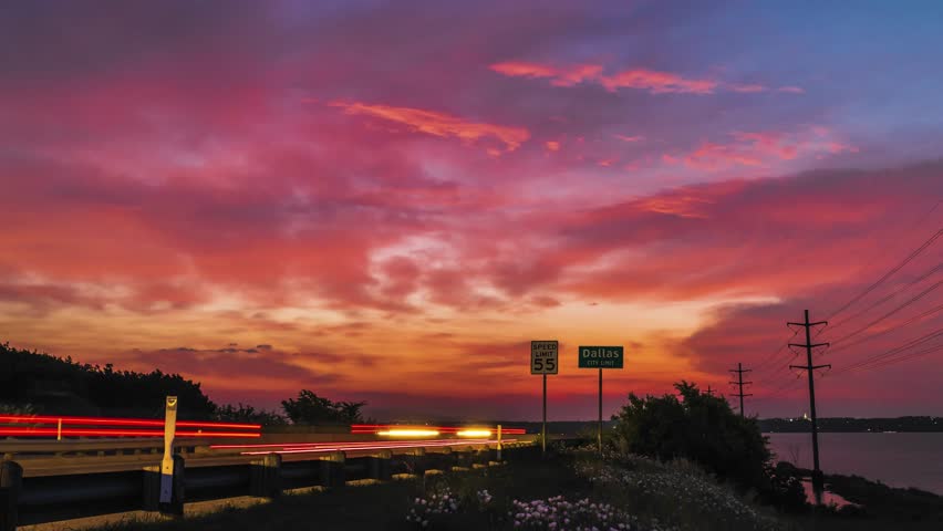 Cars zoom along highway in light trail blur in front of epic sunset sky on road to Dallas
