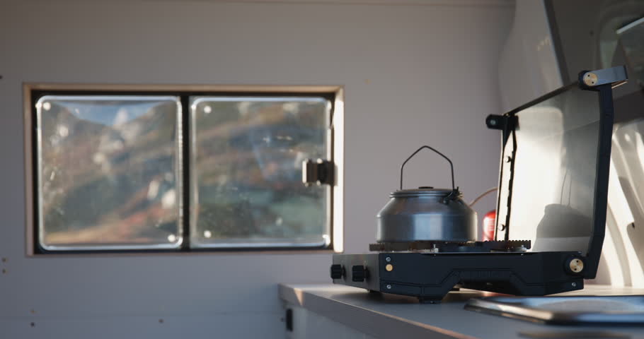 Kettle on gas burner in converted camper van with Norway mountain view; slide