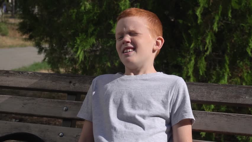 Tired thoughtful boy resting on a bench in the park