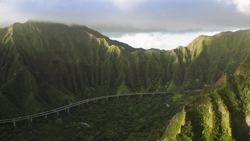 Famous mountain road with jungle nature landscape at sunrise. Scenic aerial with transportation background, travel summer trip 4K. Epic view on H-3 interstate running by cinematic Hawaii island Oahu Royalty-Free Stock Footage #1110142115