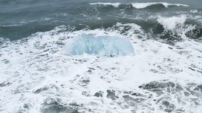 Stunning drone shot of waves breaking on a beautiful ice rock at Diamond Beach in Iceland (slow motion)