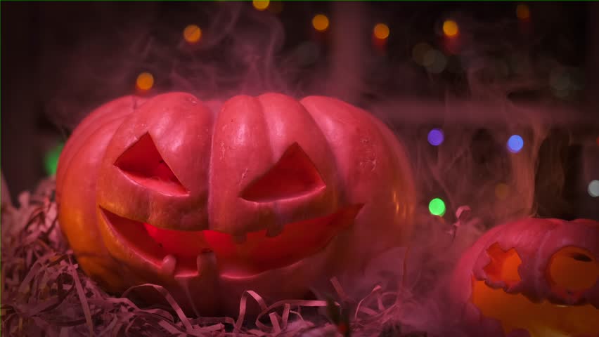 Traditional carved pumpkin with thick swirling smoke, jack o lantern lights up with flickering lights on blurred background glowing garlands at night festive background Halloween holiday, 31 October. Royalty-Free Stock Footage #1110153797
