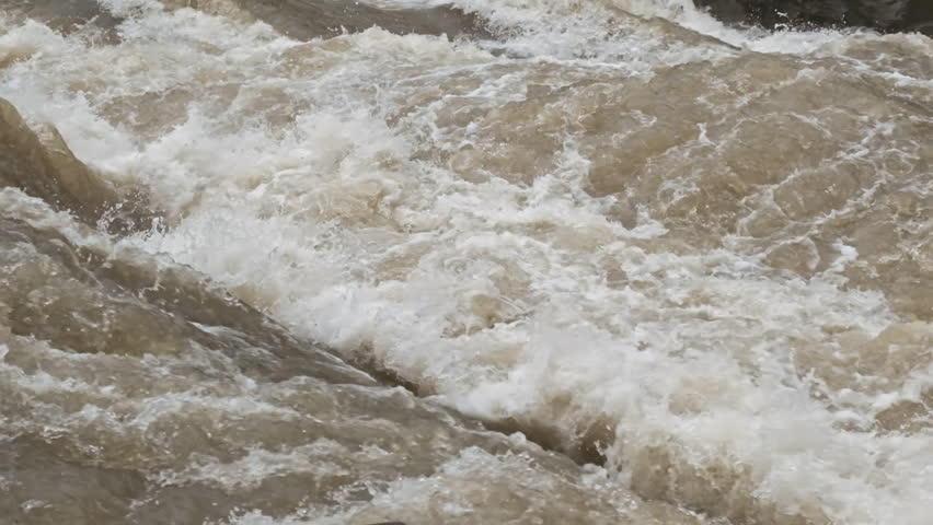 Slow motion, powerful stream of wild river water. Spring flood. Raging river flowing in wild mountains nature. Natural seething, running strong river motion. Fast speed of flow water stream splash