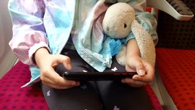 Zoom on hands of a little girl playing on her smartphone during her trip on train holding her toy.