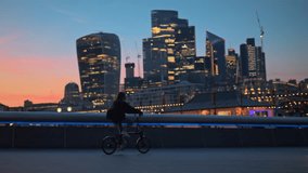 Tracking shot of young tourist woman riding bicycle towards Sky garden City of London skyline at sunset - Powered by Shutterstock - Get 15% off with code: PIKWIZARD15