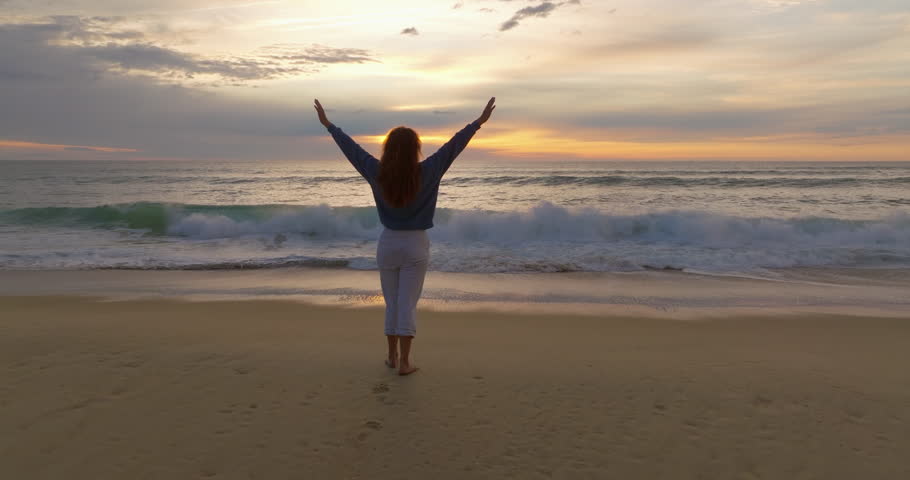 Aerial view girl with curly hair in a blue sweatshirt and gray pants runs along the surf line. Playing sports near the ocean in the fresh air. Woman feels free and happy on the beach ocean