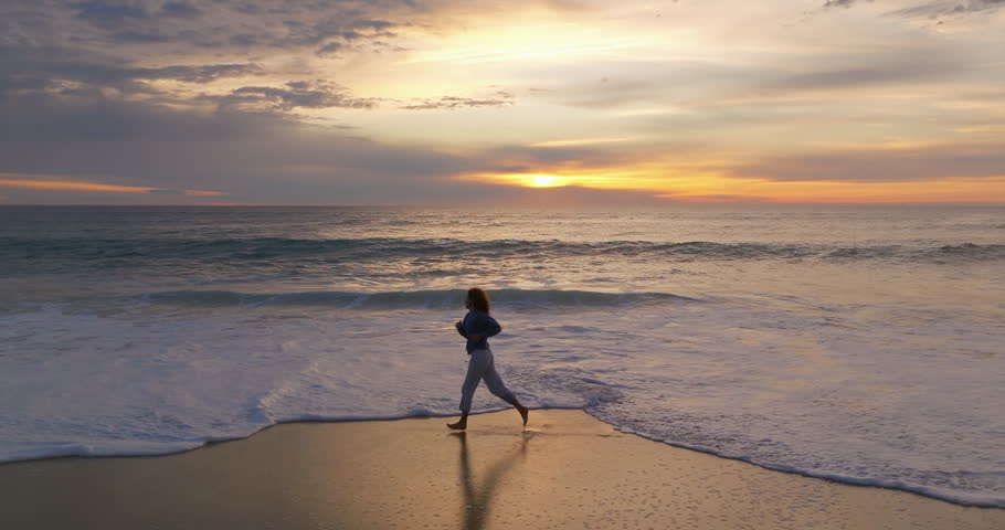 Aerial view. Beautiful woman barefoot are running In the ocean beach time evening amazing sunset, twilight