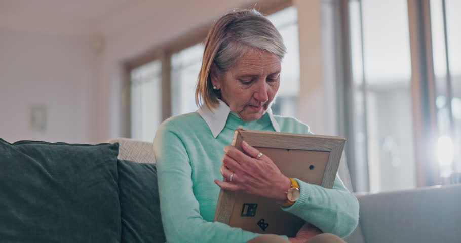 Sad senior woman, hug photo and thinking with grief, lost love and broken heart on living room sofa in home. Elderly lady, picture frame and depression for death, mourning and memory on lounge couch