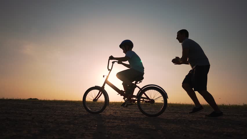 Father's Day. Father teaches son to ride bicycle wearing safety helmet. child learn to ride bicycle in park at sunset. Happy family concept and dream. Active father teaches child to ride bike in park Royalty-Free Stock Footage #1110169447
