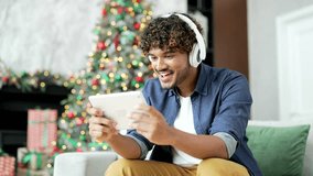 Excited young man in wireless headphones watching sports match competition on a tablet sitting at home during winter New Year Christmas holidays. Happy guy watches video stream or plays a game online - Powered by Shutterstock - Get 15% off with code: PIKWIZARD15