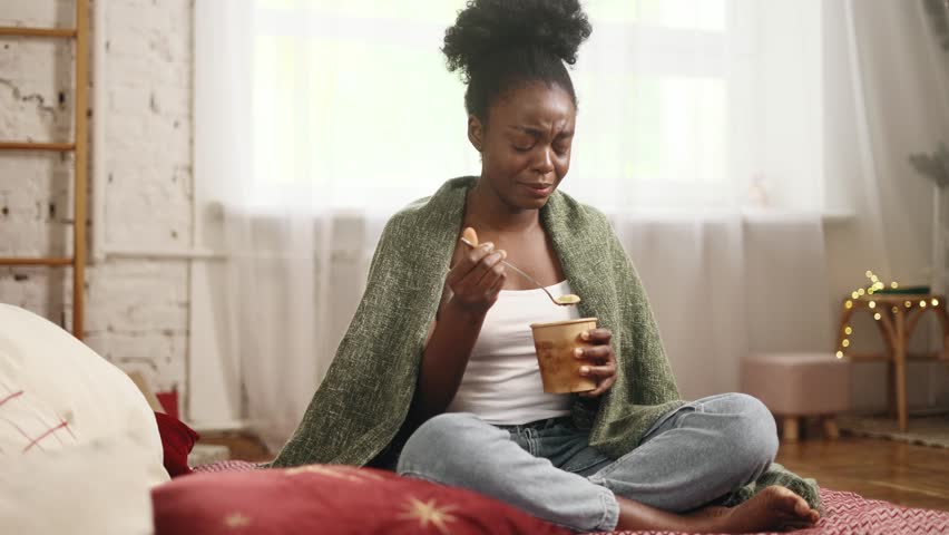 Portrait of sad young woman dealing with stress by eating food sitting on bed at home Upset brunette female wrapped in blanket crying and eating ice cream indoors alone Mental heath problem Royalty-Free Stock Footage #1110177489