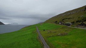 Backward drone over Kirkjubour village on Faroe Islands with cabins in meadow on foggy day