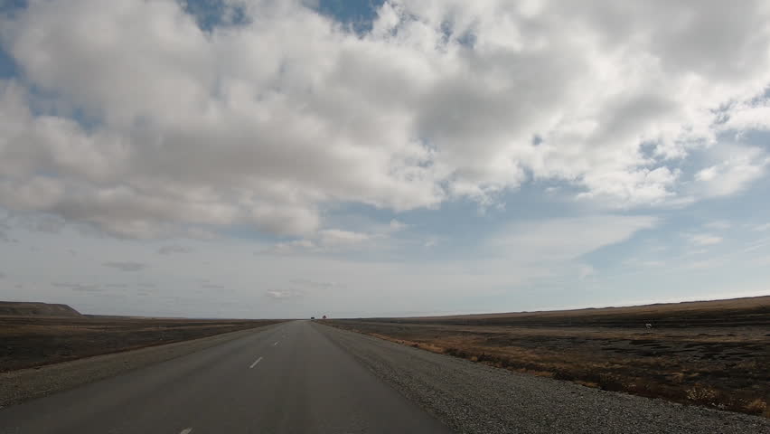 Pov of a cari driving across the countryside field under a dramatic sky with clouds