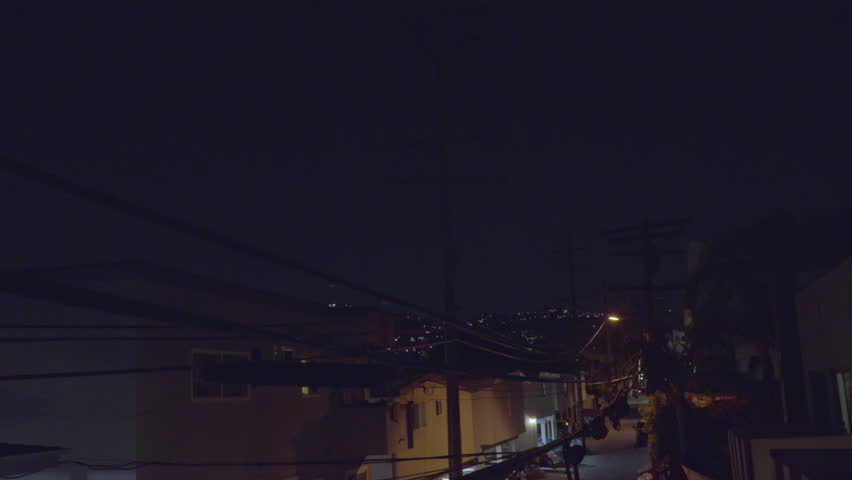 Camera dolly down to reveal West Hollywood alley at night in Los Angelas, California. Camera moves next to powerlines and has warm and cold lighting contrast. 