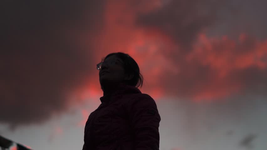 Silhouette of Indian teenager girl looking at orange sky during sunset at Manali, Himachal Pradesh, India. Hopeful girl stares at the sky. Female lost in deep thoughts after looking at the sunset.