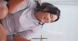 Vertical clip. A chubby Asian woman enjoying pizza while relaxing on the sofa at home.