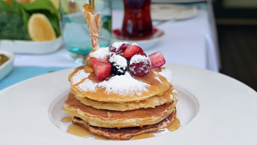Syrup is poured over the pancakes. Stack of pancakes with strawberries, blackberries and maple syrup Royalty-Free Stock Footage #1110186229