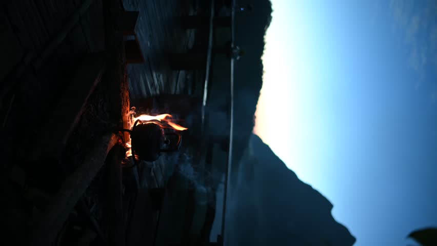 Old small kettle is heated on a bright bonfire on mountain in the rays of rising sun stunning morning during travel. Mountain Sunrise Adventure