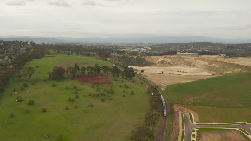 The camera captures an aerial view of a train running between a green, lush landscape and an open pit mine, presenting a picturesque scene. Royalty-Free Stock Footage #1110188199