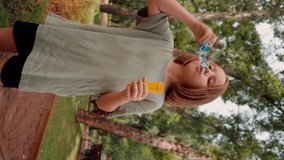 vertical video portrait beautiful cute little girl blowing soap bubble in city park happy carefree childhood