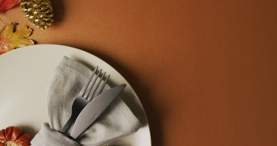 Animation of friendsgiving text over cutlery and autumn leaves over brown background. Thanksgiving, american tradition and celebration concept digitally generated video.