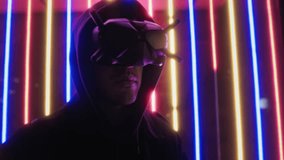 Portrait of man wearing hoodie and virtual reality headset standing on street of neon flashing multicolored lights in background in dark night. Futuristic technology, cyberpunk atmosphere - Powered by Shutterstock - Get 15% off with code: PIKWIZARD15