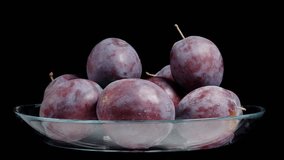 Plums in a glass bowl. They rotate on a black background, looped video, isolated.