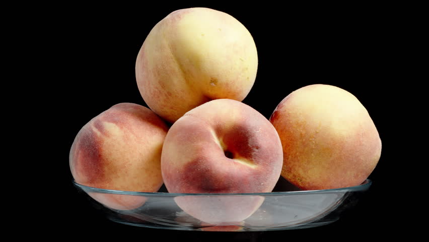 Large peaches in a glass bowl. They rotate on a black background, looped video, isolated.