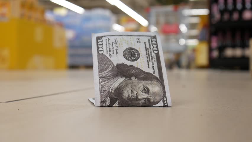 Close-up of a lost hundred dollar bill lying on the floor and a man with a shopping trolley finds it