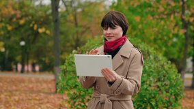 Portrait of business lady using tablet computer in autumn park. Young attractive woman looking at tablet screen outdoors. Elegant business woman using online with digital device outside. Fashion, girl