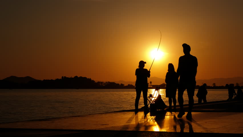 Popular fishing hobby in evening. A view of people silhouette enjoy the popular fishing hobby on the sunset beach in summer.