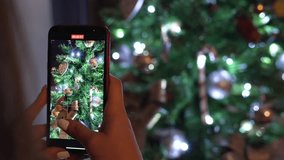 Hands of young girl recording a video with her cell phone of the Christmas tree. Close up video of unrecognizable person making a video of his personal Christmas celebration with lights twinkling.