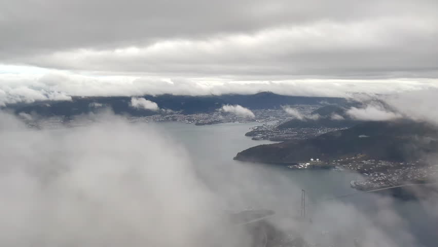 Final approach before landing in Bergen, Norway, shot from airplane with view of downtown Bergen between the clouds