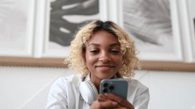 Happy dark skinned girl using smartphone for dating app,online shopping,messaging,watching videos