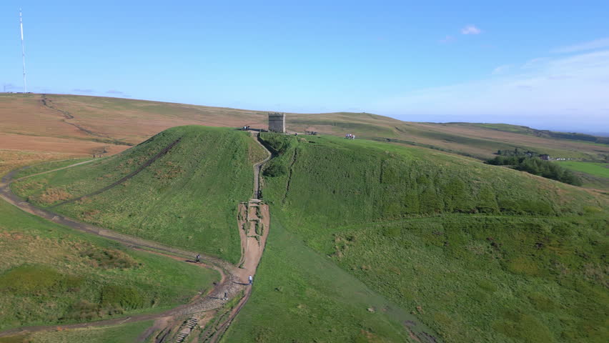 Stone structure on hilltop with orbit revealing autumnal colours of moorland and tall radio transmitters on hill behind. Rivington, Lancashire, England, UK.