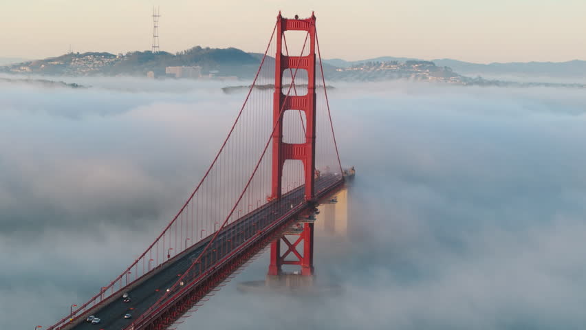 Cinematic view of red Golden Gate Bridge in scenic Karl fog at sunrise. San Francisco drone footage, California 4K. Aerial over Golden Gate with city of San Francisco on background, West Coast USA