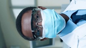 Portrait of African American scientist with medical mask and goggles glancing at camera. Wearing white medical coat while standing in modern laboratory. Observing safety measures around lab. - Powered by Shutterstock - Get 15% off with code: PIKWIZARD15