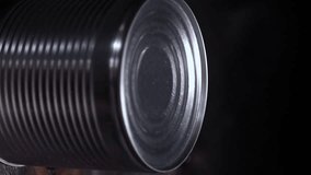 Close-up strong male hands with a can opener make an incision on the lid of a metal can on a black table, vertical video