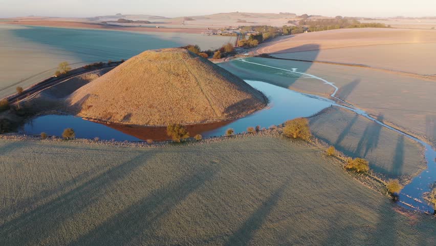 Aerial of Neolithic Silbury Hill, UNESCO World Heritage Site, on a frosty winter morning, with flooding around the mound, Wiltshire, England, United Kingdom, Europe