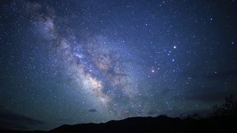 motion controlled astrophotography time lapse footage with dolly down, tilt, pan right & zoom in motion of Milky Way galaxy over desert landscape through dawn in Death Valley National Park, California